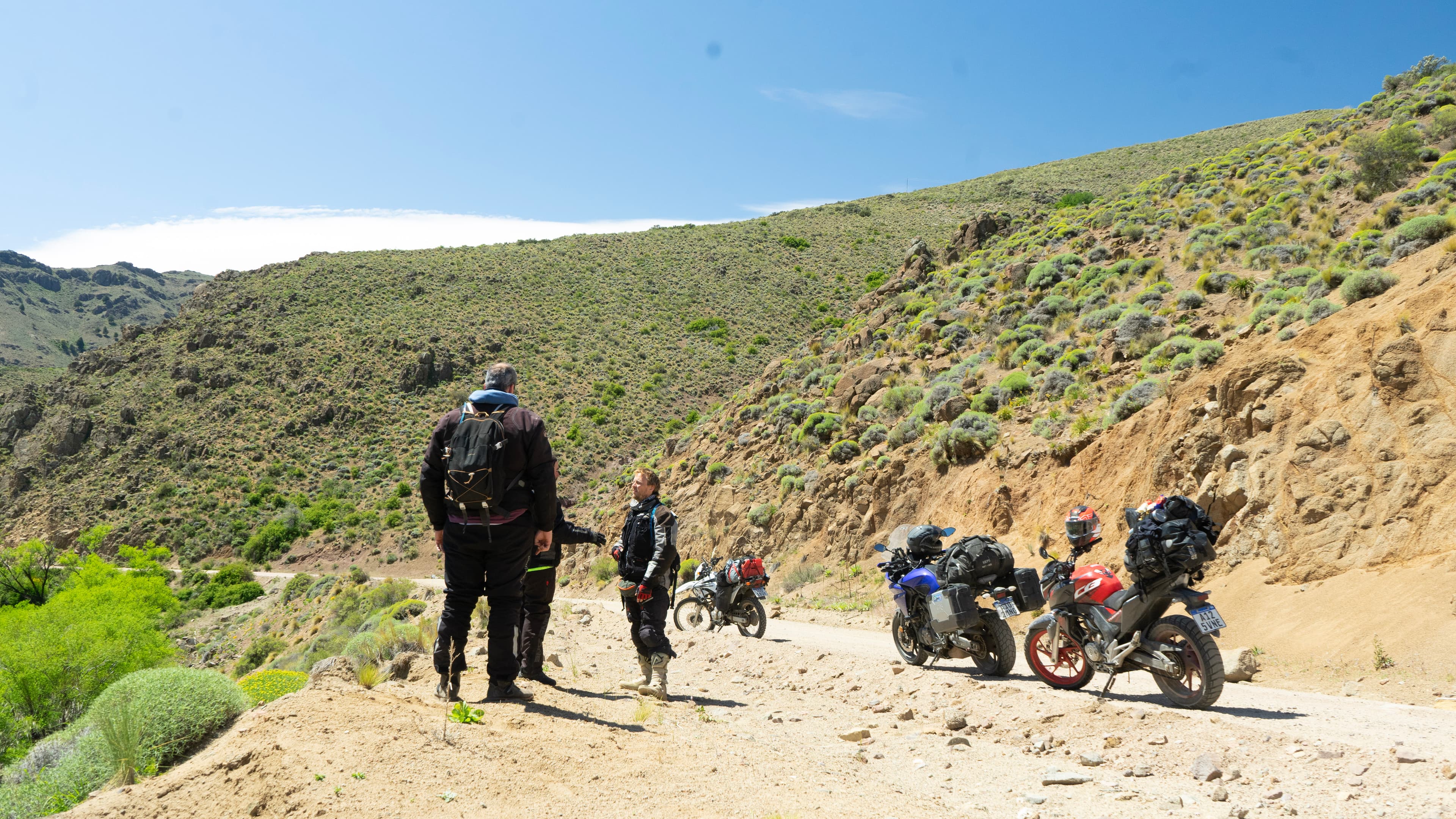 Riders beside loaded motorcycles on a gravel road during Cruces del Sur.