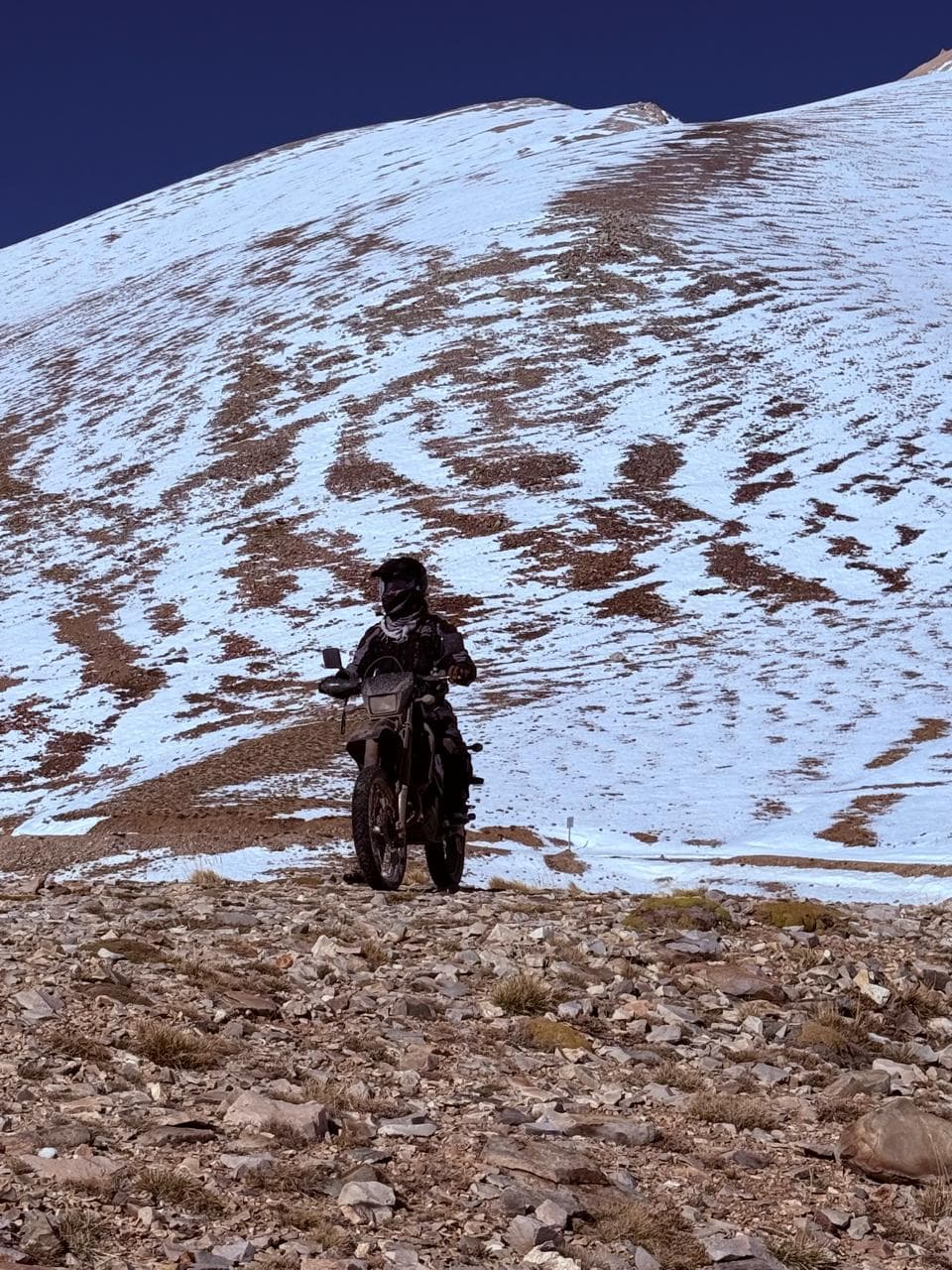 Piloto en moto atravesando una ladera nevada en alta montaña.