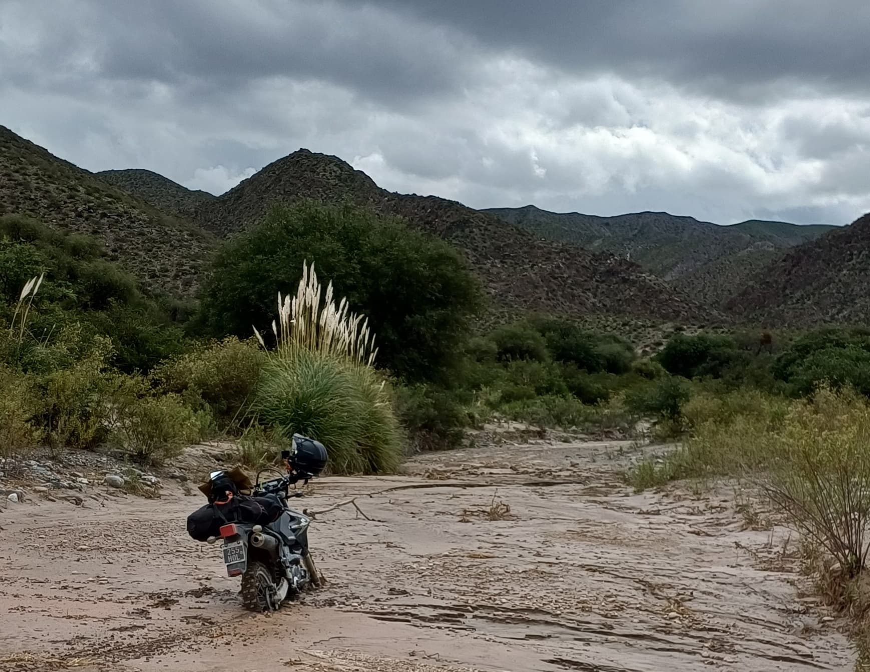 Motorcycle stopped on a sandy road under storm clouds in Catamarca.